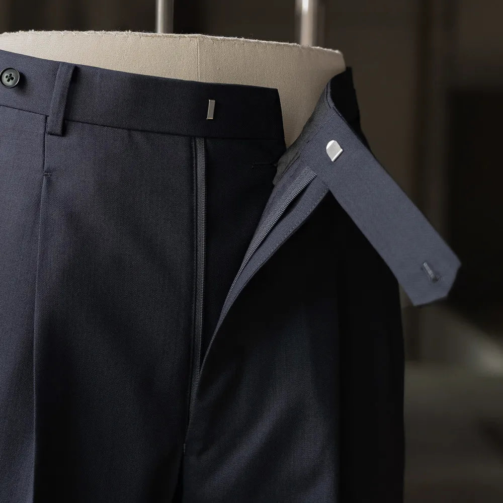 Detail of the trousers’ front closure showing the waistband, extension tab, and interior finishing.