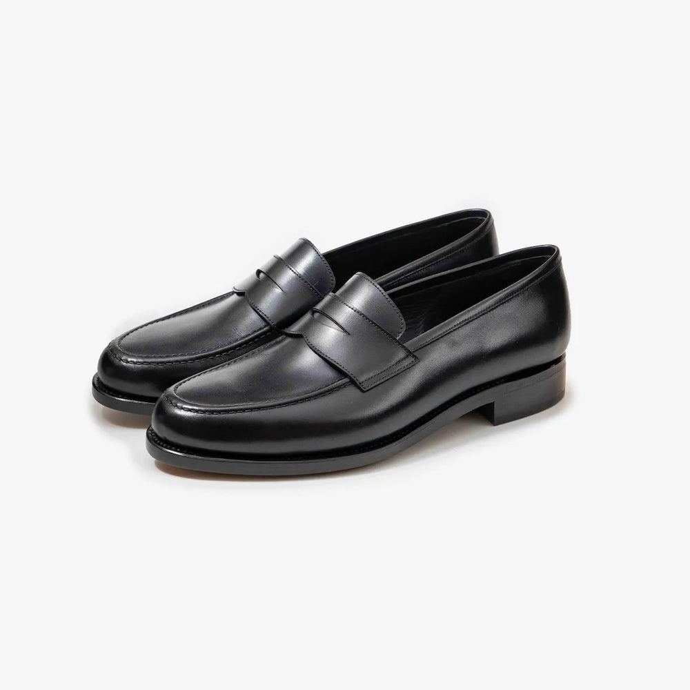 A pair of TLB Mallorca 718 Queens Penny Loafers in black box calf leather, shown at an angle to highlight the elegant silhouette and polished finish.