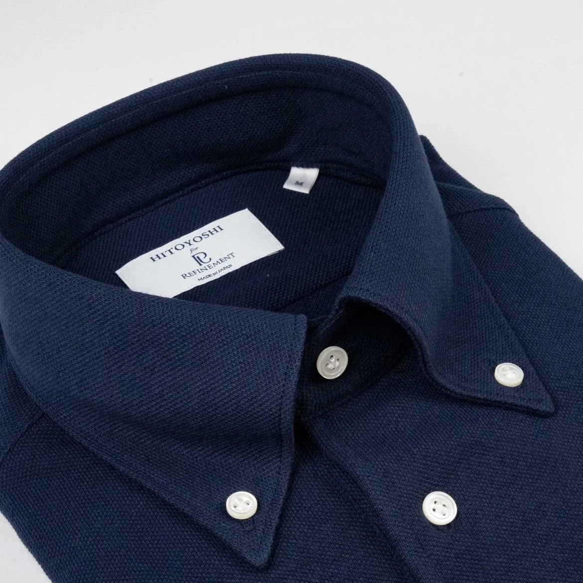 Close-up of the button-down collar showing roll shape, stitching precision, and refined knit texture.
