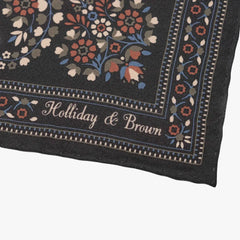 Close-up of the Holliday & Brown grey pocket square corner showing the printed border, paisley details, and brand logo.