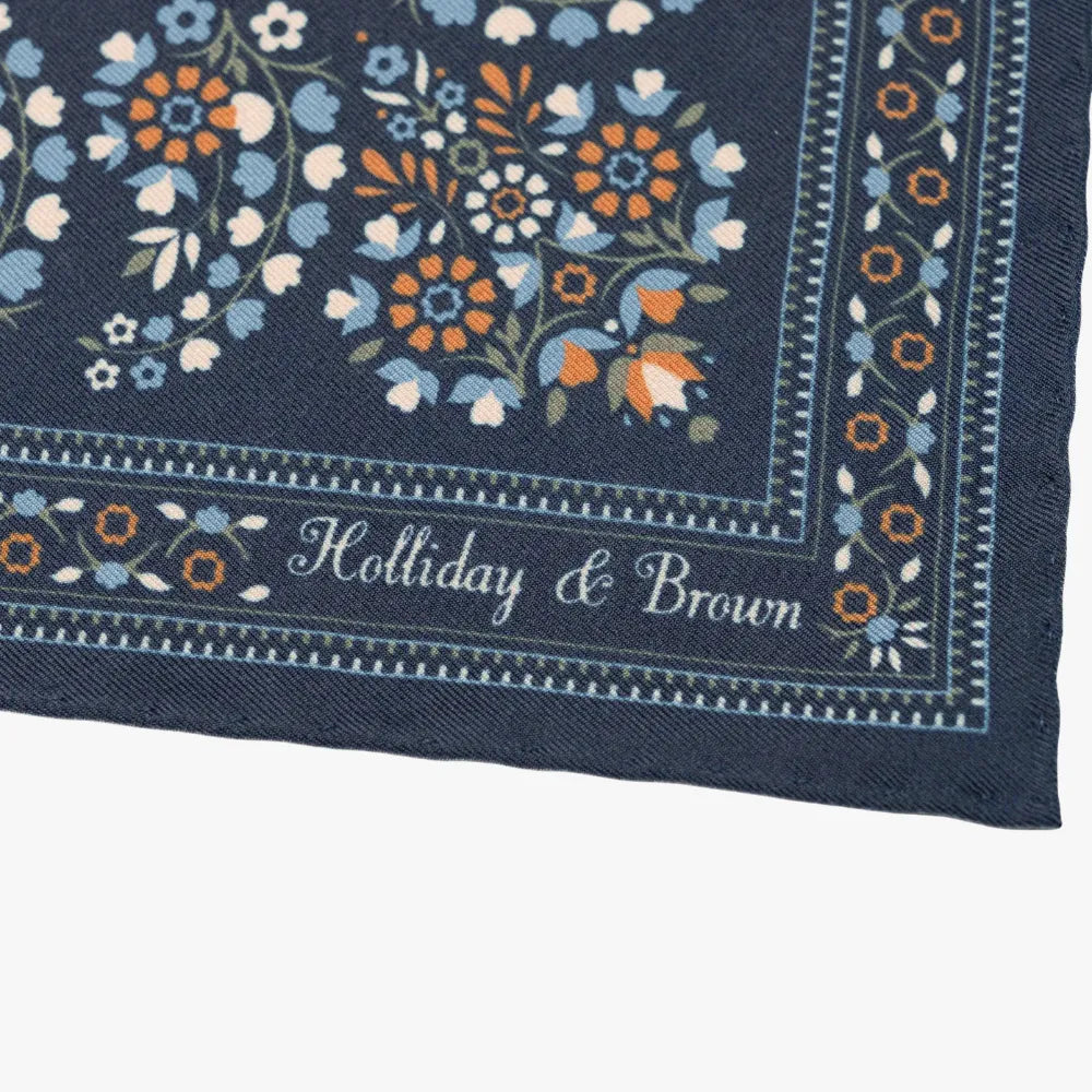 Close-up of the Holliday & Brown navy pocket square corner highlighting the brand logo, crisp border print, and pattern detailing.