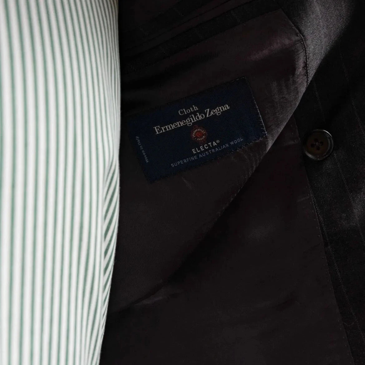 Close-up of the interior labels on the RMJ-04 Chalk Stripe Charcoal Grey Suit showing Refinement Made By Ring Jacket branding and Ermenegildo Zegna Electa fabric label.