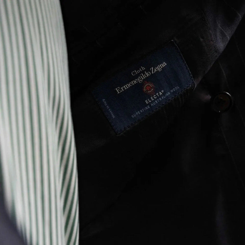 Close-up of the interior labels on the RMJ-04 Chalk Stripe Navy Suit showing Refinement Made By Ring Jacket branding and Ermenegildo Zegna Electa fabric label.
