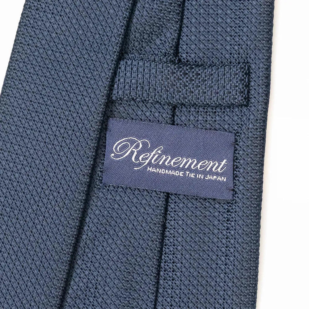 Close-up of the Refinement plain neck tie showing refined silk weave and brand label detail.