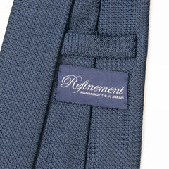 Close-up of the Refinement plain neck tie showing refined silk weave and brand label detail.
