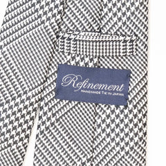 Close-up of the Refinement Prince of Wales neck tie showing the textured silk weave and brand label detail.