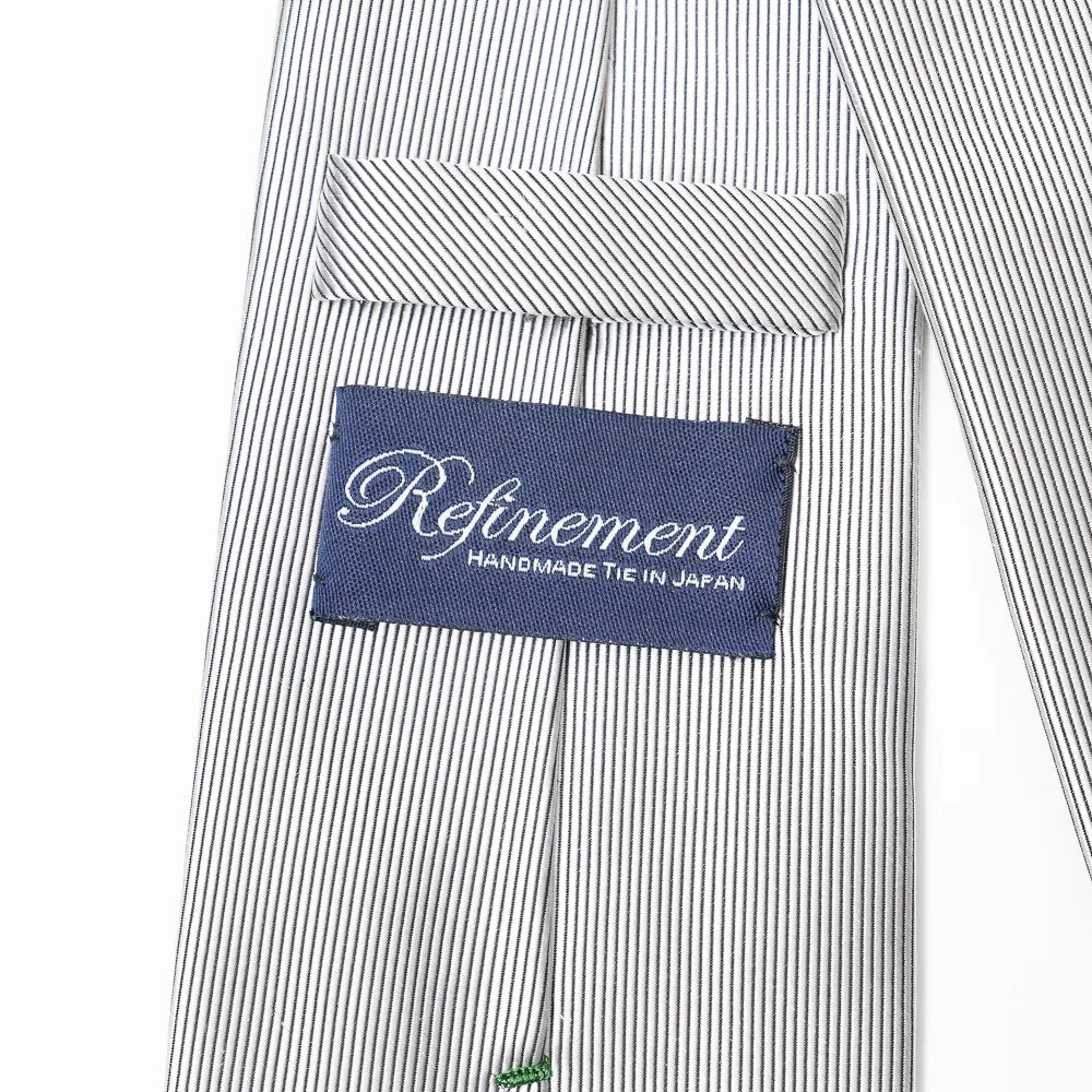 Close-up of the Refinement stripe neck tie showing textured silk weave and brand label detail.
