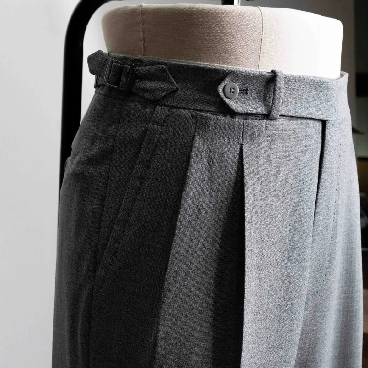 Close-up of the waistband showing button closure, belt loops, stitching precision, and sartorial construction.