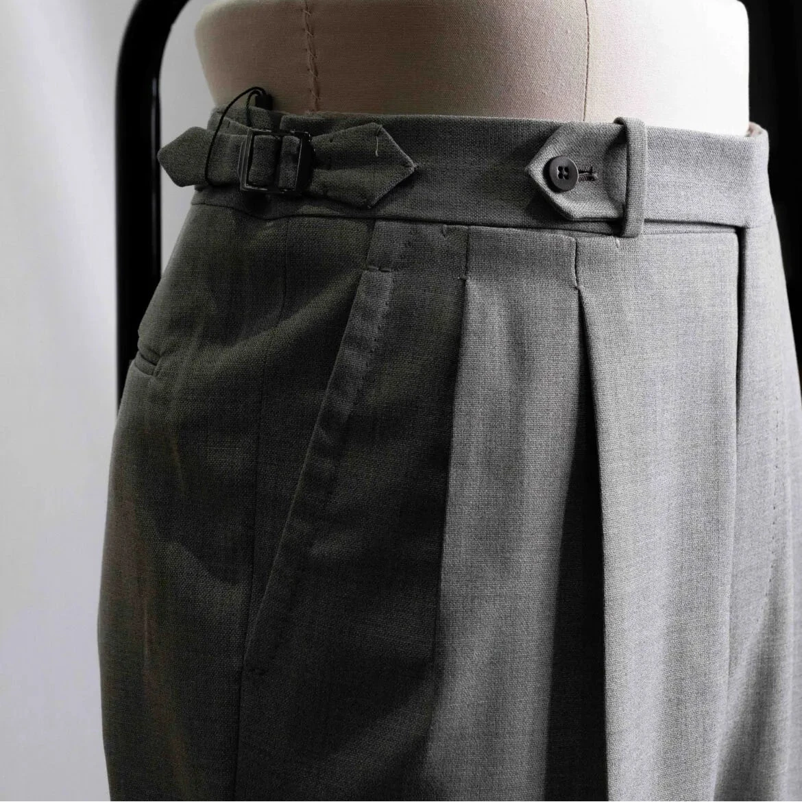 Close-up of the waistband showing button closure, belt loops, stitching precision, and sartorial construction.