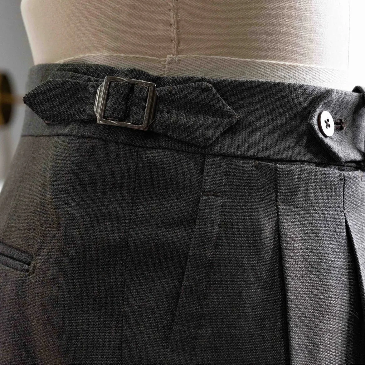 Close-up of the waistband showing button closure, belt loops, stitching precision, and clean sartorial construction.