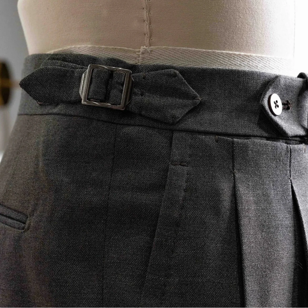 Close-up of the waistband showing button closure, belt loops, stitching precision, and clean sartorial construction.