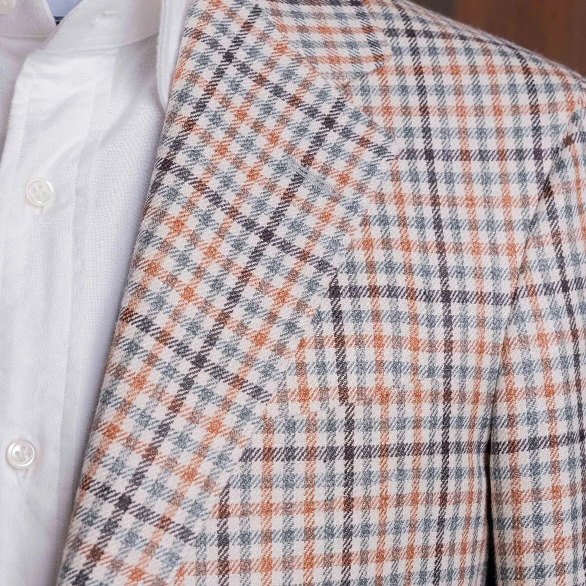 Close-up of the lapel showing the notch construction, pick stitching, and the detailed beige gun club weave from E. Thomas.