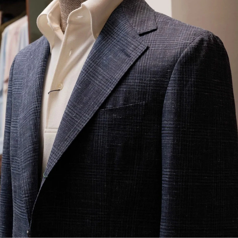 Close-up of the lapel showing notch lapel construction, pick stitching, and the detailed navy glen check weave from Fratelli Tallia di Delfino.
