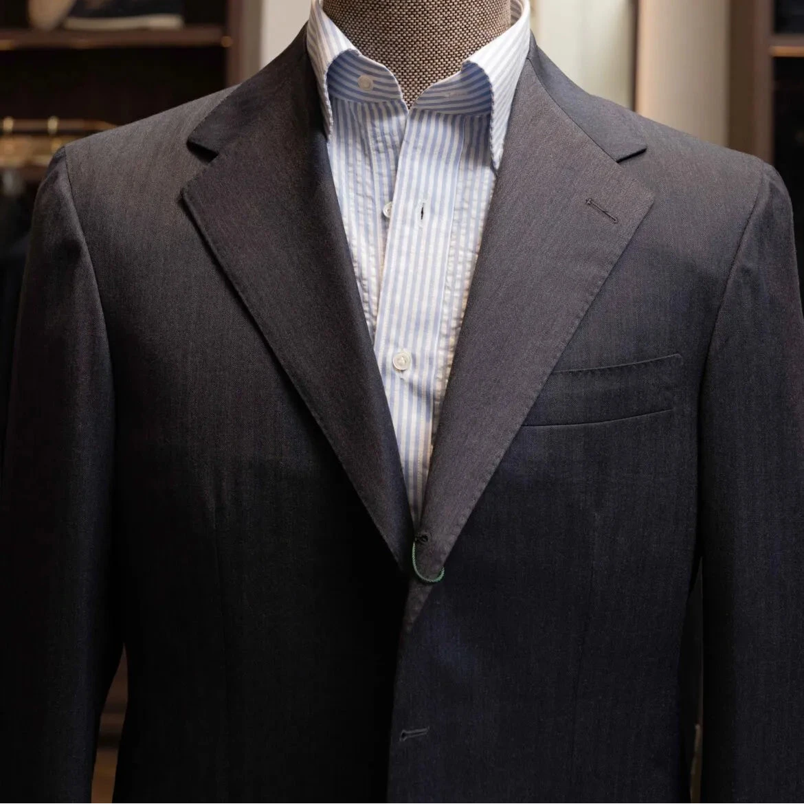 Close-up of the notch lapel showing pick stitching and the detailed Savile Clifford navy-grey herringbone weave.
