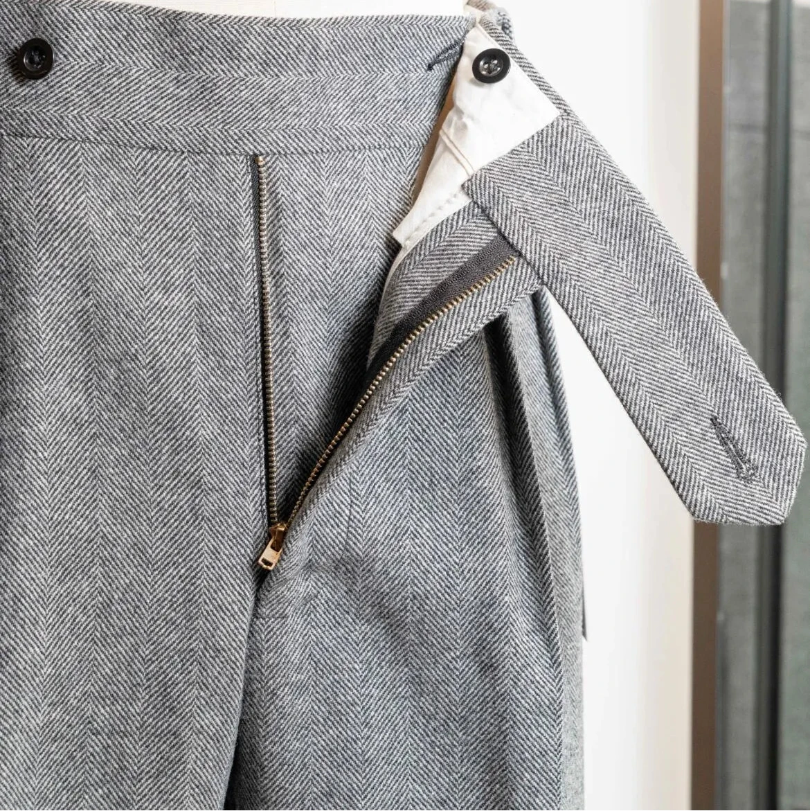 Close-up of the waistband of the Tangent TAN02 Henry Hard Classic Tweed Herringbone Light Grey trousers showing adjusters and button details.