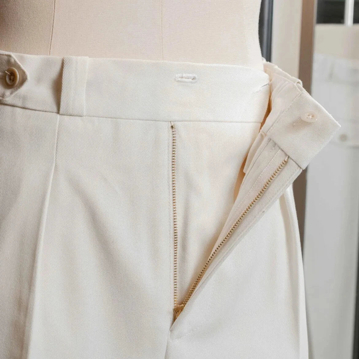 Close-up of the waistband of the Tangent Tan 04° Charles Hard Twist Twill Off White trousers, showing the side adjusters and button details.