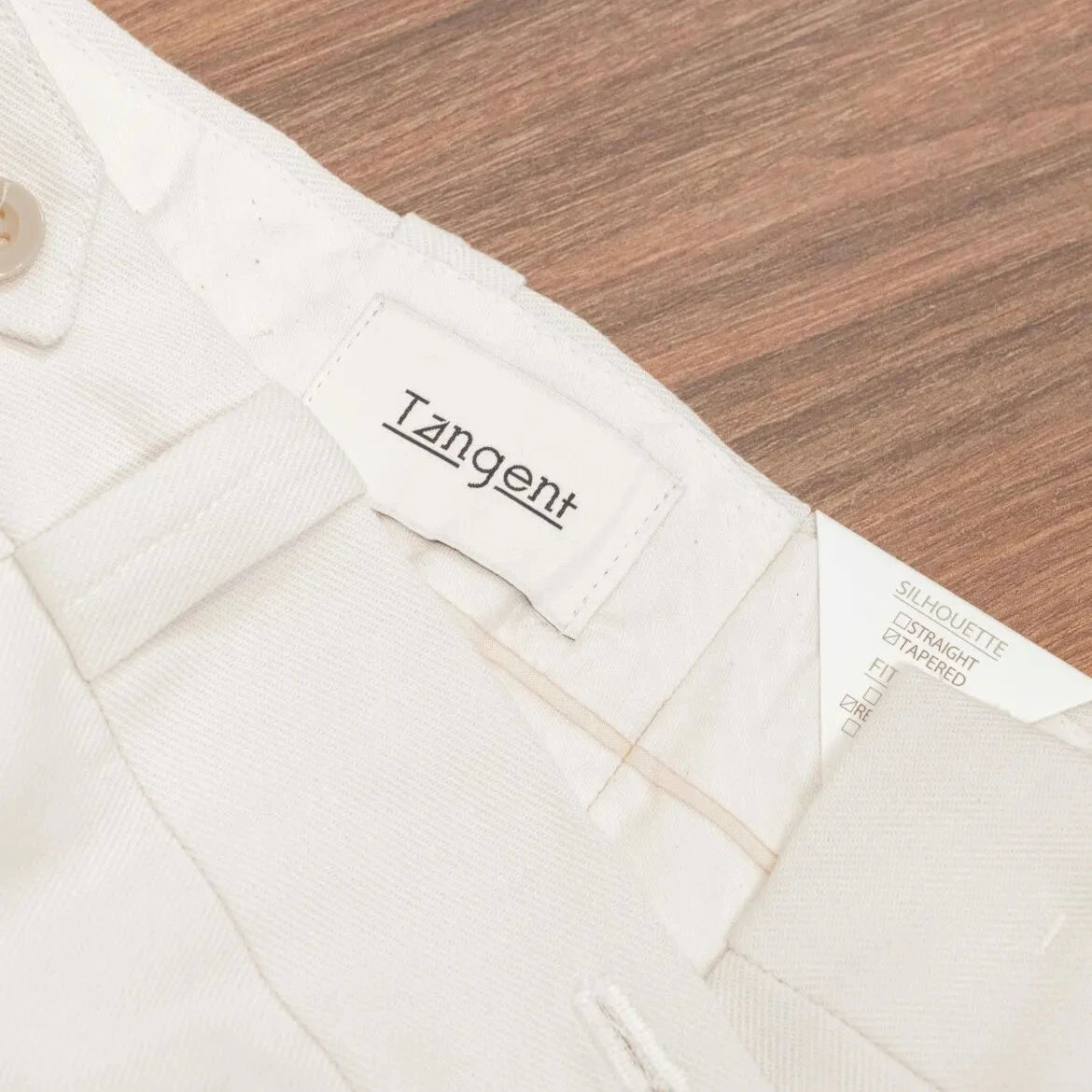 Close-up of the inner label of the Tangent Tan 04° Charles Hard Twist Twill Off White trousers showcasing branding and construction.