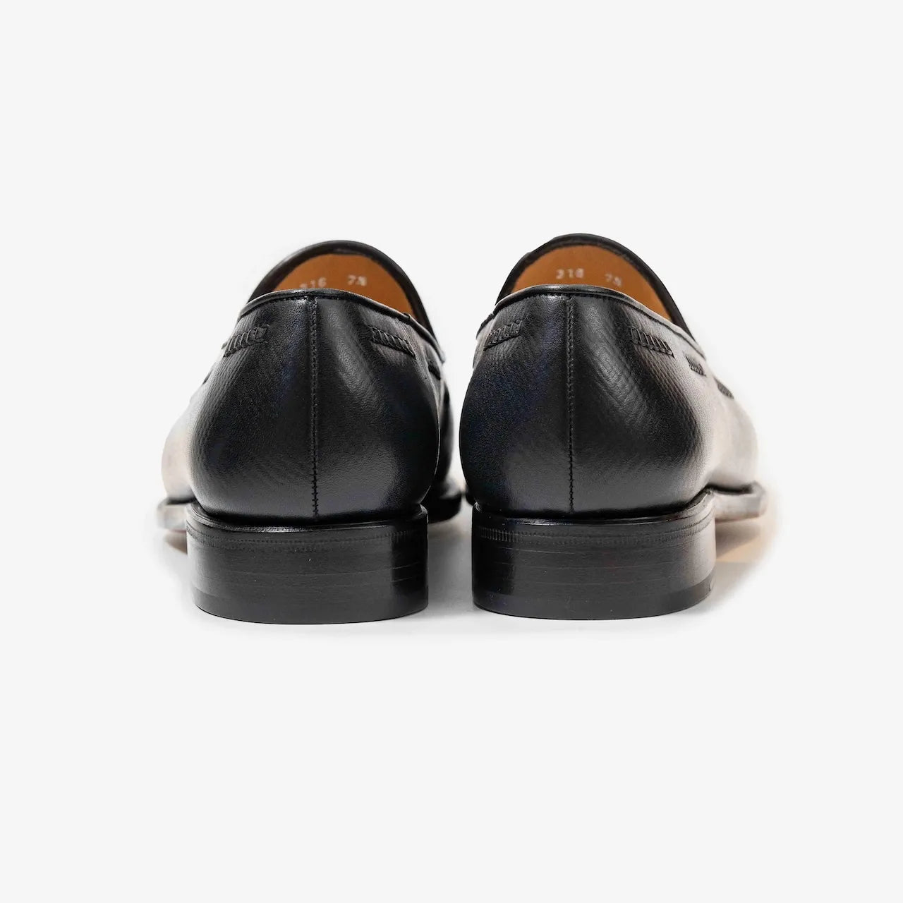 A pair of black hatch grain leather tassel loafers from TLB Mallorca, shown at an angle to highlight the texture and design.