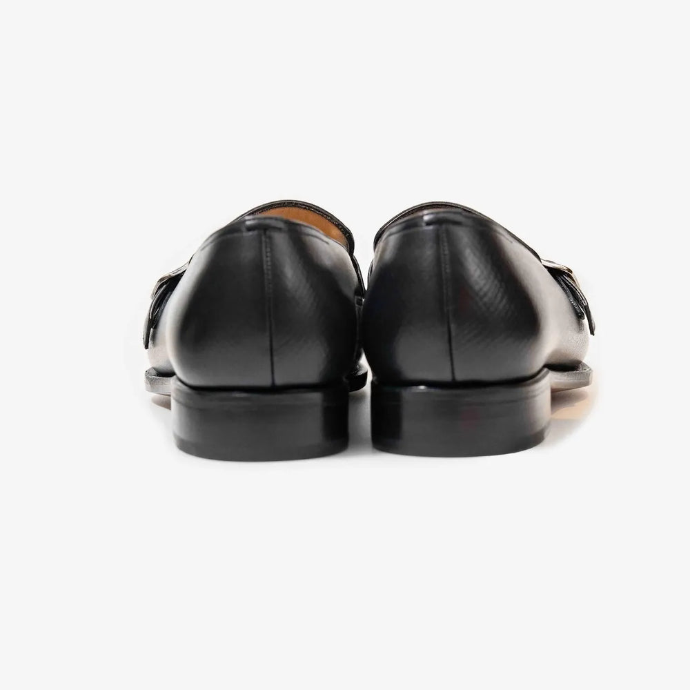 Rear view highlighting the heel shape and fine stitching of the black hatch grain buckled loafers.