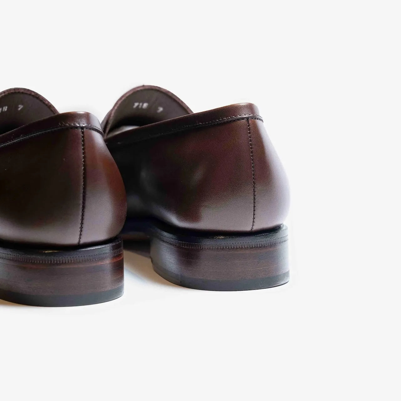 Rear view highlighting the heel curve and craftsmanship of the dark brown vegano penny loafers.